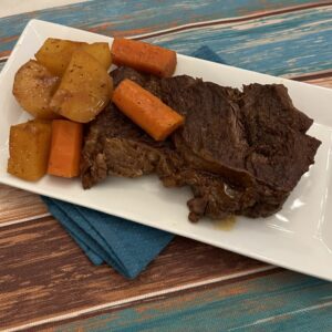 A plate of Dutch oven chuck roast with chunks of yellow potatoes and carrots, served on a rectangular white dish with a colorful wooden table mat underneath.