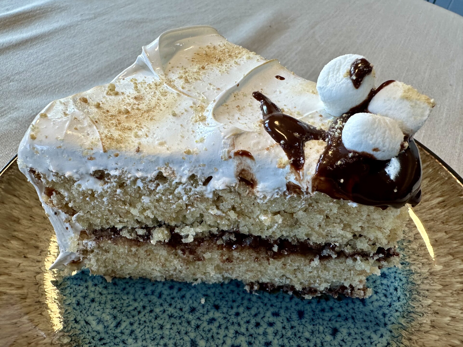 A slice of s’mores cake topped with marshmallow fluff, chocolate ganache, and mini marshmallows.