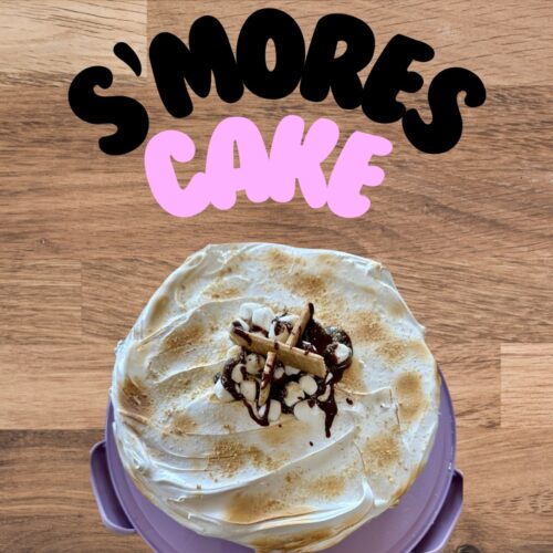 S’mores cake topped with marshmallows, chocolate, and graham crackers on a purple platter.