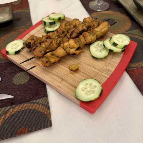 Grilled chicken satay skewers served on a bamboo cutting board with fresh cucumber slices, perfect for appetizers or a dinner party.